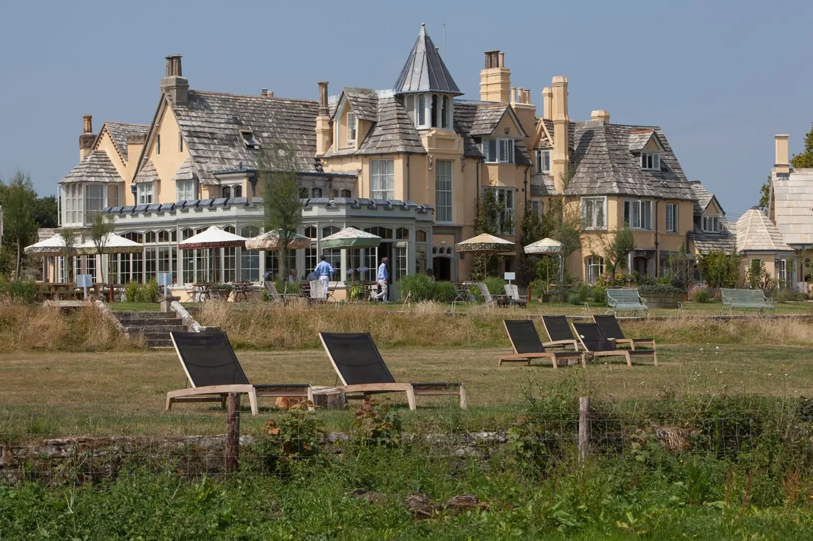 The mellow-yellow Gothic Revival house seen across the lawn, with sun loungers on the grass